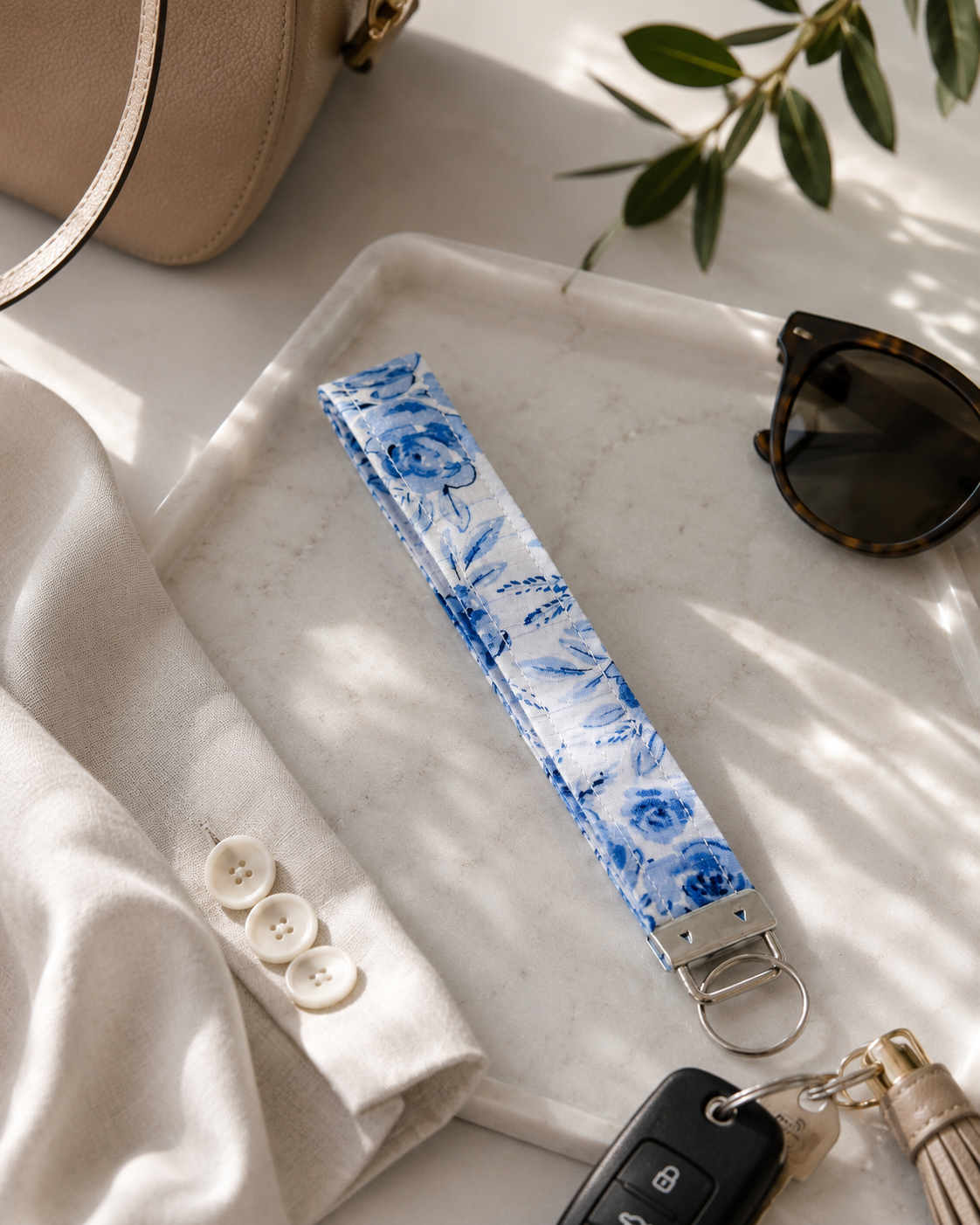 Blue Blossom quilted key fob wristlet styled with car keys, sunglasses, and a neutral handbag on a marble tray.