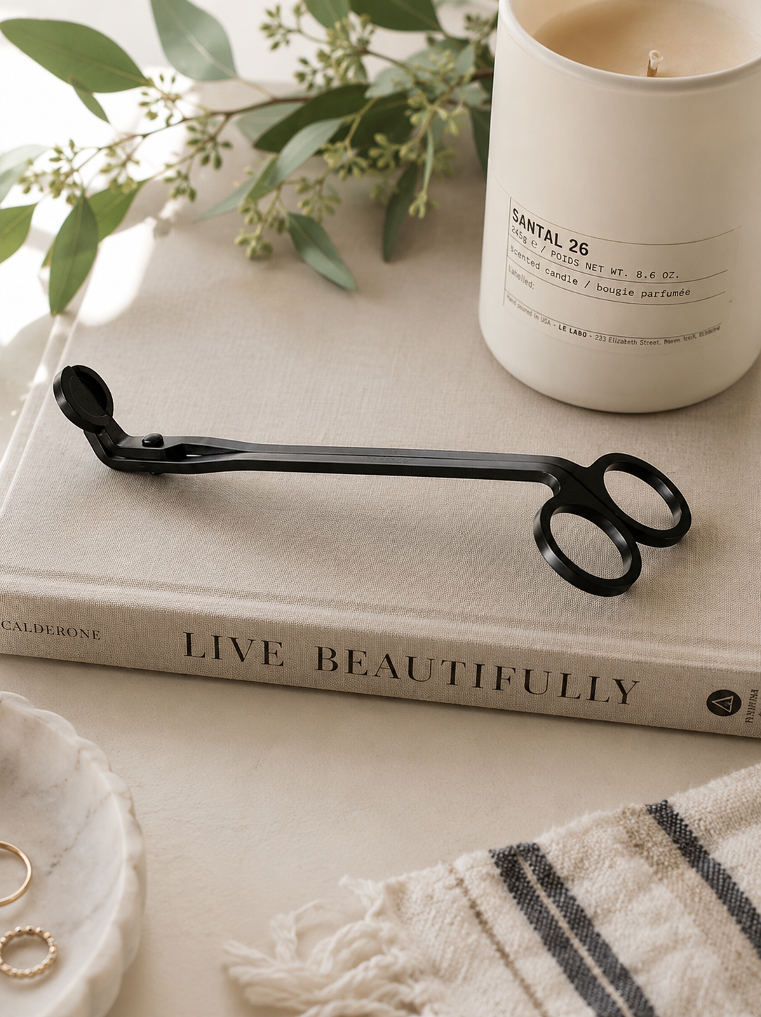 Matte black candle wick trimmer styled on stacked coffee table books beside a lit candle in a modern California-inspired living room.