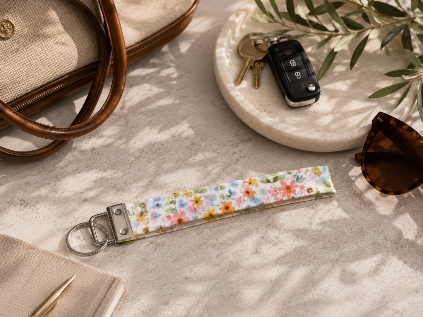Petals & Posies floral key fob wristlet styled with car keys, sunglasses, and a neutral handbag on a stone tabletop.