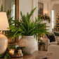 Real Touch Norfolk Pine stems styled in a rustic ceramic vase on a wooden entryway console with warm, elegant Christmas decorations.