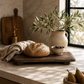 Rustic elevated wood board styled with artisan bread, olive branches, linen textiles, and ceramic accents in a warm California modern kitchen.