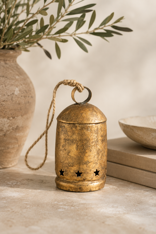 Antique gold holiday bells in assorted sizes styled on a reclaimed wood console with cedar garland, vintage landscape artwork, stoneware vase, and warm designer holiday décor.