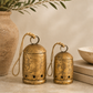 Large and medium antique gold hanging bells with distressed finish and star cutout details styled together in a warm designer holiday vignette with olive branches, neutral books, and natural stone accents.