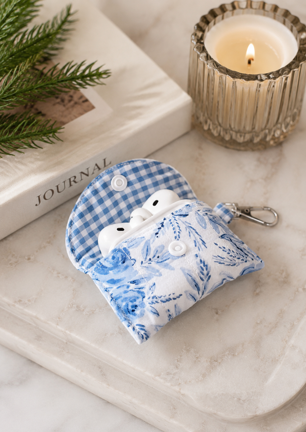 Blue Blossom quilted AirPods case styled on a marble tray with wireless earbuds in a soft modern lifestyle setting.