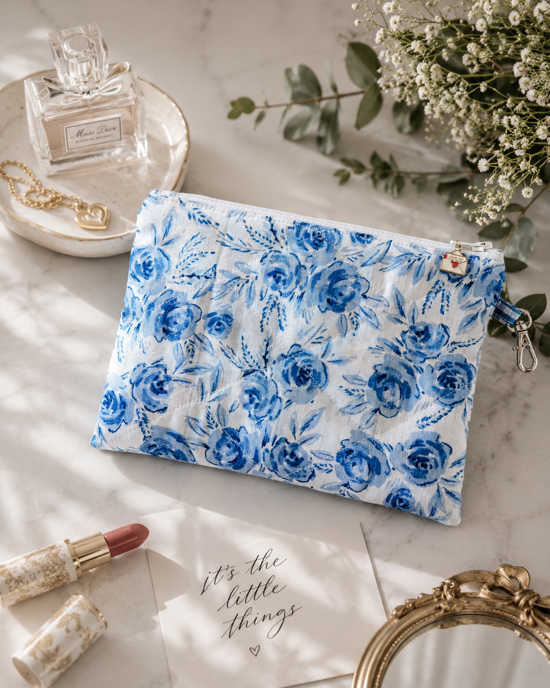 Blue Blossom quilted medium wristlet pouch styled with everyday essentials including cards, lip gloss, and personal accessories.