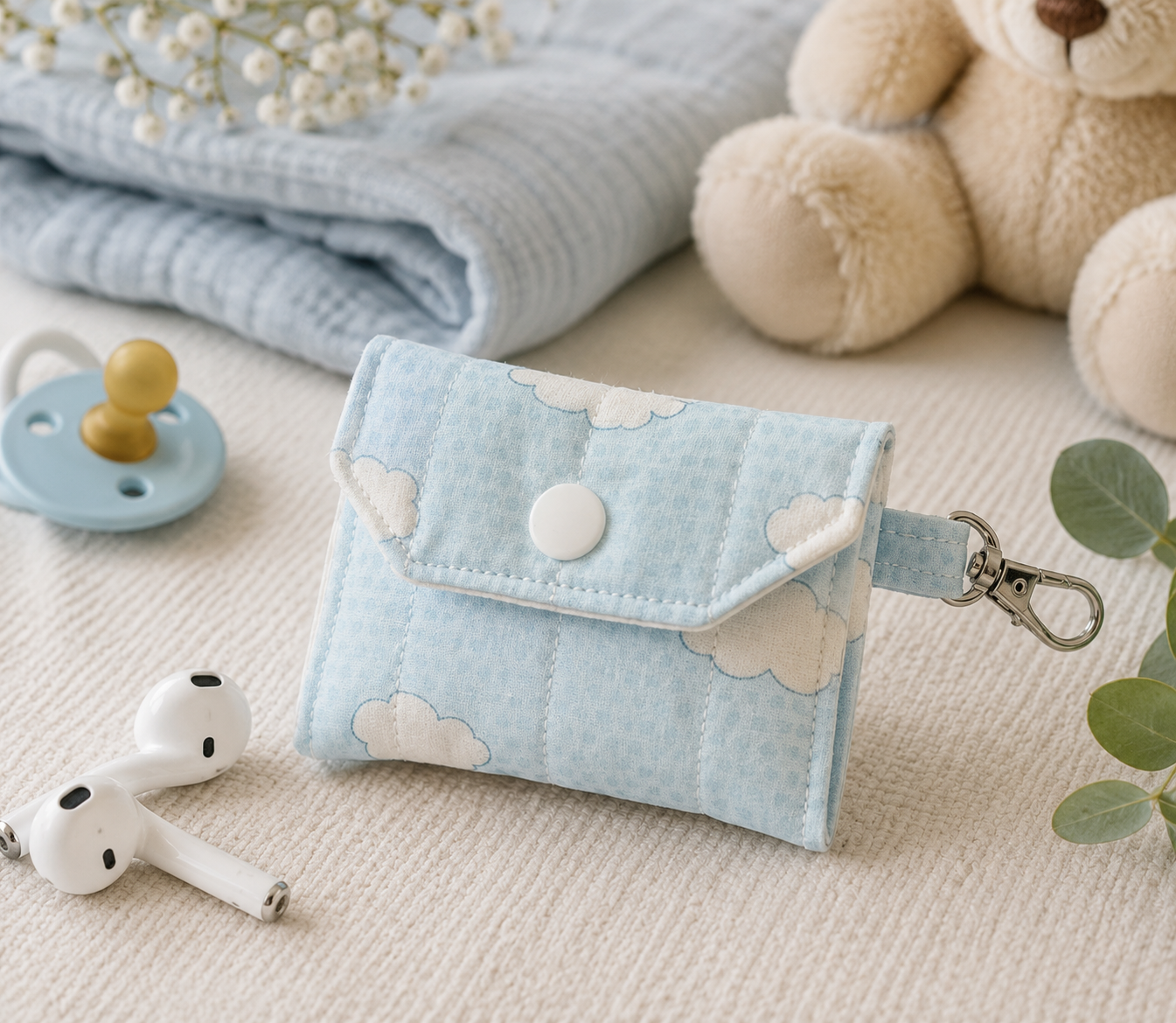 Blue Skies quilted AirPods case with soft blue cloud print and coordinating blue gingham accent, styled with wireless earbuds in a nursery-inspired setting.