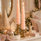 Set of two blush pink Christmas tree-shaped taper candles featuring delicate layered branches, displayed in antique brass candle holders against an elegant ivory marble studio background.