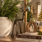 Standing and grazing burnished iron reindeer sculptures styled together on a wooden console with Norfolk pine greenery and timeless neutral Christmas decorations.