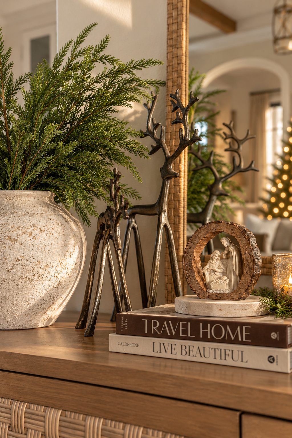 Standing and grazing burnished iron reindeer sculptures styled together on a wooden console with Norfolk pine greenery and timeless neutral Christmas decorations.