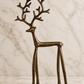 Standing burnished iron reindeer sculpture with tall branching antlers, slender legs, and an antiqued bronze-brown finish, photographed on an elegant ivory marble studio background.