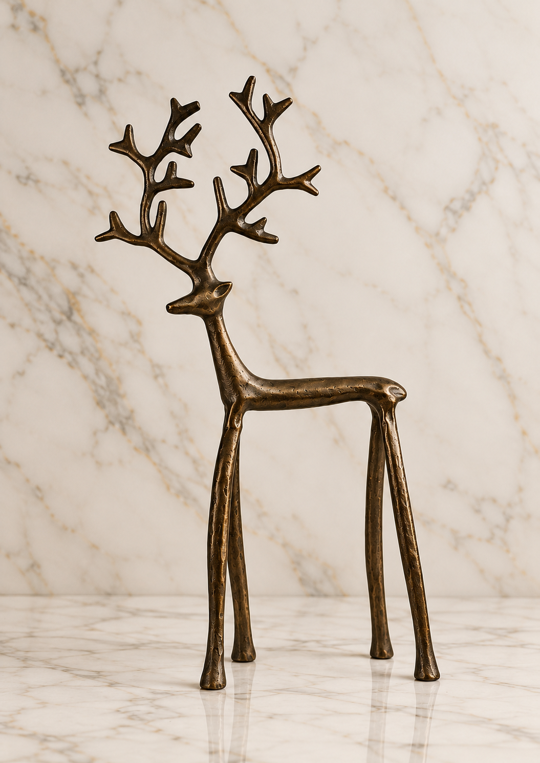 Standing burnished iron reindeer sculpture with tall branching antlers, slender legs, and an antiqued bronze-brown finish, photographed on an elegant ivory marble studio background.
