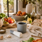 Small gray speckled ceramic mortar and pestle styled on a creamy marble countertop with heirloom tomatoes, basil, lemons, olive oil, and rustic bread in a warm California-modern summer kitchen.