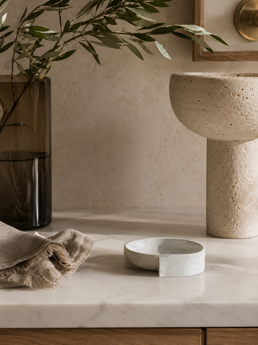 Minimal cement soap dish styled on creamy marble with warm brass accents, olive branches, smoked glass, and spa-inspired California modern decor.