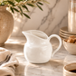 White ceramic pitcher on a marble surface with a neutral color palette