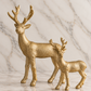Set of two champagne gold reindeer sculptures in coordinating sizes, featuring textured metallic finishes and branching antlers on an ivory marble studio background.