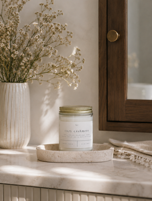 Cozy Cashmere soy candle styled on a bathroom vanity with a ceramic vase, greenery, and warm brass accents.