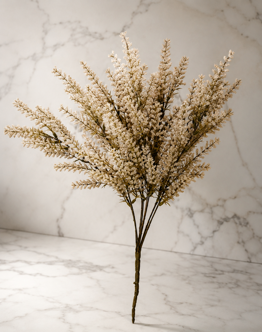 Cream faux astilbe stem displayed against a white marble studio backdrop, highlighting its realistic texture and soft neutral color.