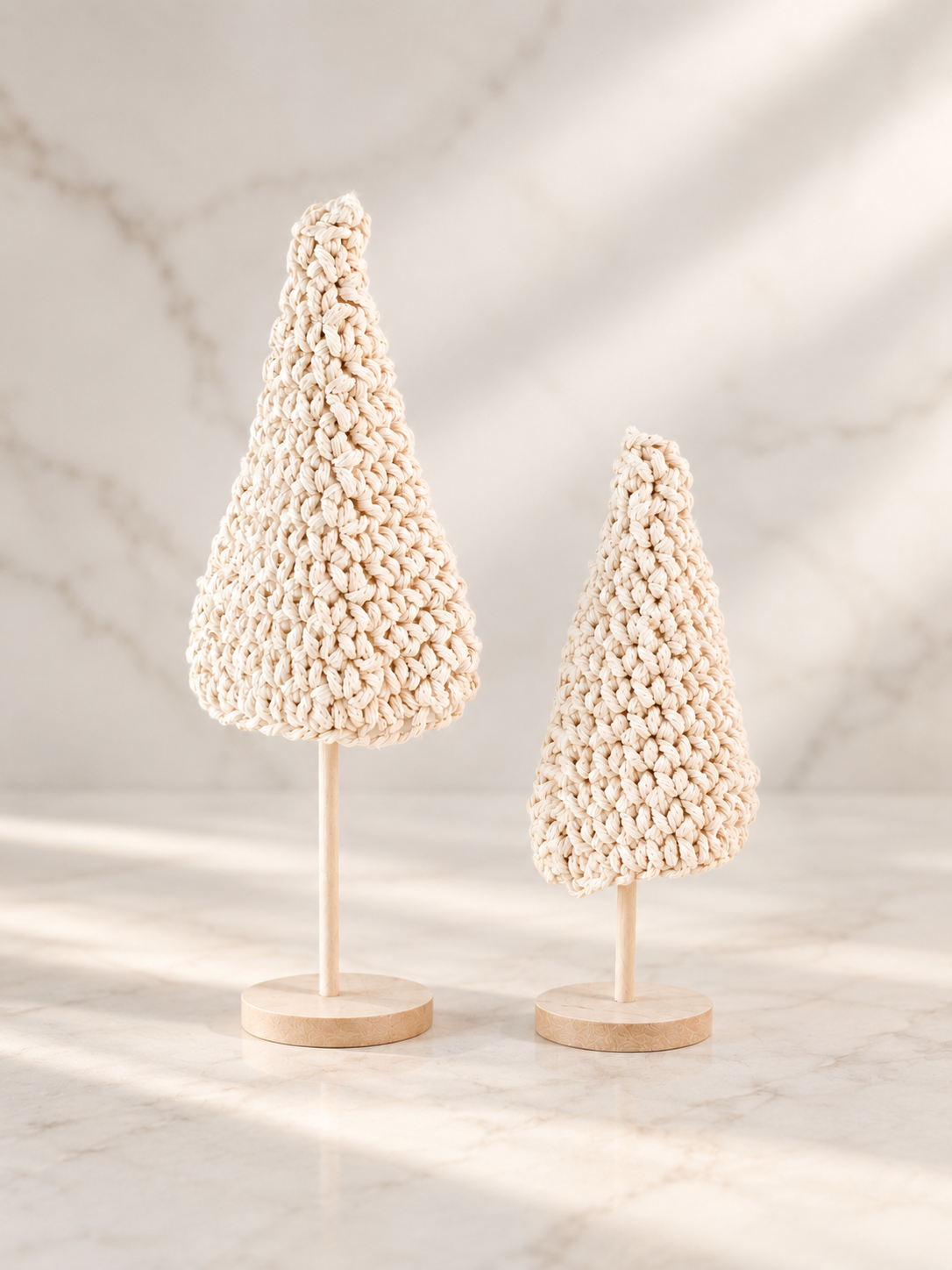 rochet Christmas trees on natural wood stands styled against a soft neutral marble backdrop.