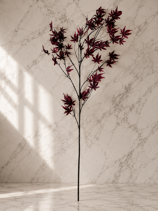 Dark red faux maple leaf stem displayed against a white marble studio backdrop, highlighting its natural branching, rich burgundy leaves, and realistic texture.