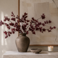 Dark red faux maple leaf stems arranged in a ceramic vase on a stone console light painting and modern organic décor.