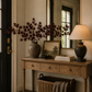 Dark red faux maple leaf stems arranged in a ceramic vase on a warm wood entryway console with a brass mirror and modern organic décor.