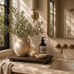 Rustic decorative wood board styled on a luxury bathroom vanity with olive branches, candlelight, stone accessories, and warm brass fixtures.