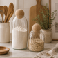 Glass storage jars with cork ball lids styled on a modern kitchen countertop with flour, rolled oats, natural wood accents, and ceramic kitchen décor.