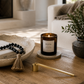 Gold candle snuffer styled on a wood coffee table beside a lit candle, decorative bowl, and greenery in a modern California-inspired living room.