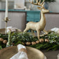 Gold finish decorative plate styled on a holiday tablescape with a white napkin, greenery garland and a gold reindeer centerpiece