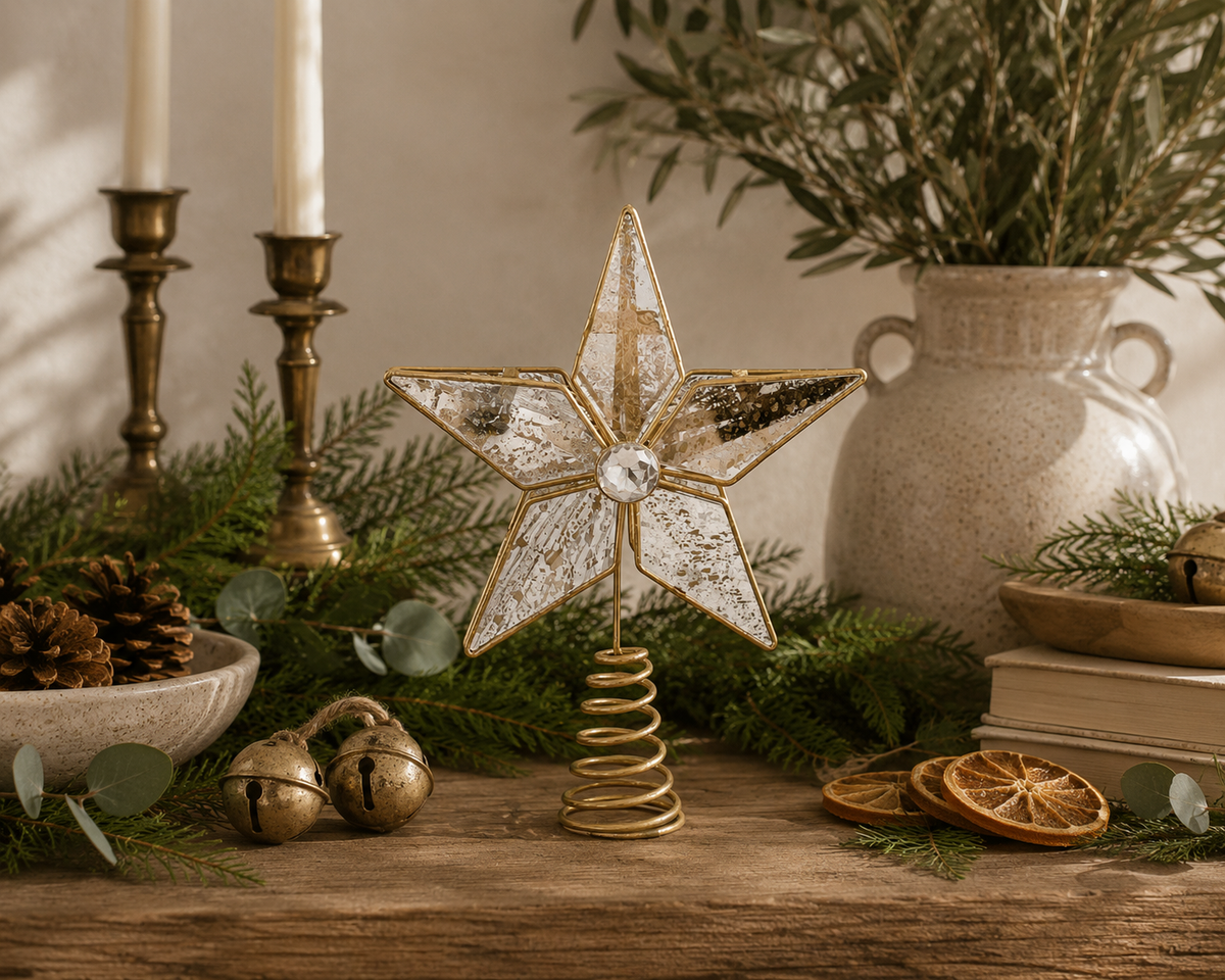 Gold mercury glass star tree topper with antiqued mirrored glass panels and crystal center styled on a reclaimed wood console with cedar greenery, brass candlesticks, pinecones, dried orange slices, and designer-inspired Christmas décor.
