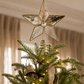 Gold mercury glass star tree topper with antiqued mirrored glass panels and crystal center displayed atop a beautifully decorated Christmas tree with warm white lights, velvet ribbon, and neutral designer-inspired holiday ornaments.
