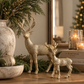 Two champagne gold reindeer figurines styled on a warm wood console table with natural greenery and neutral Christmas accents.