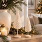 Cream hand-crocheted Christmas trees on wood stands styled with evergreen garland and neutral holiday décor.