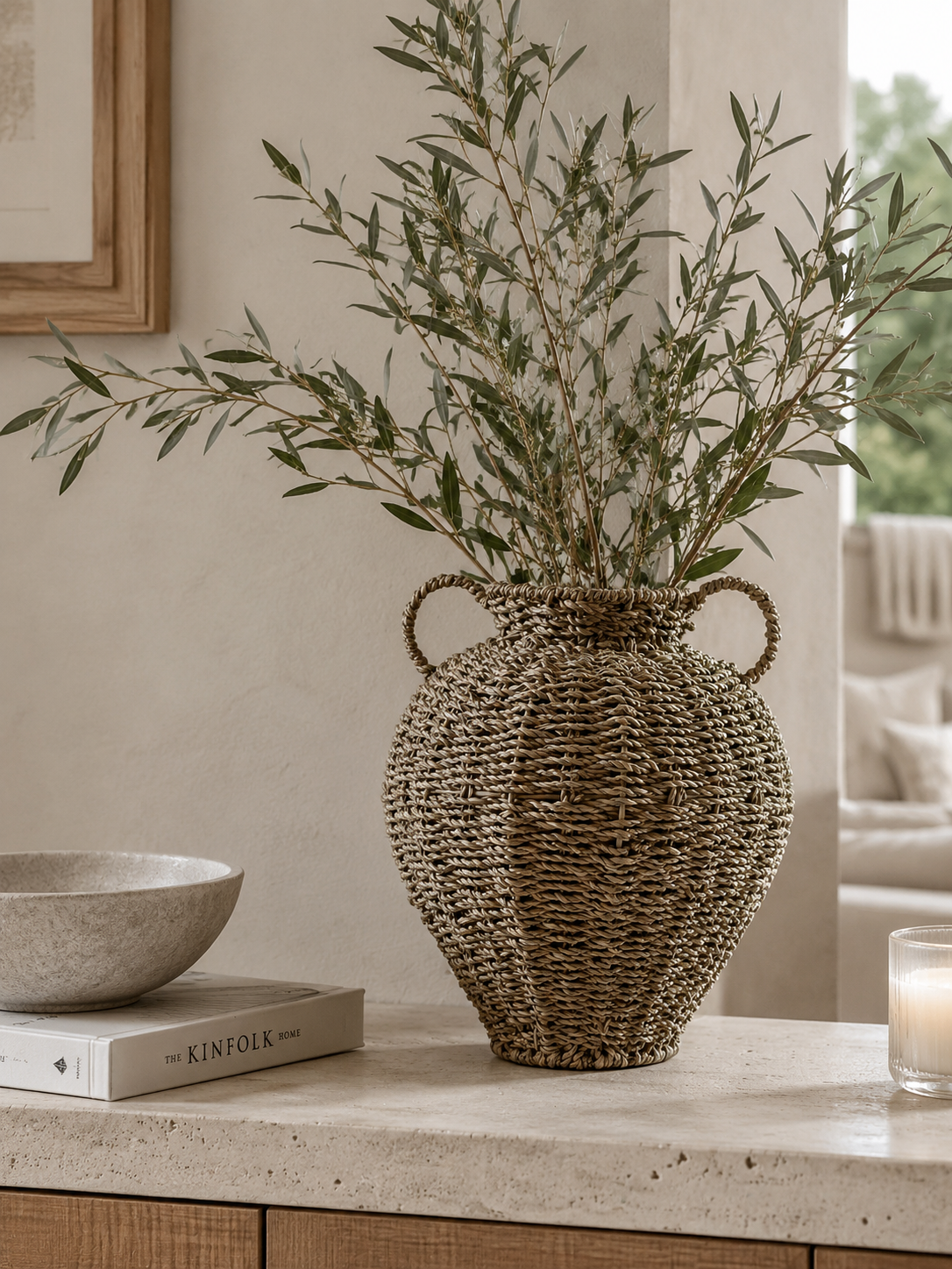 Decorative woven vase with green branches on a table in a room setting.