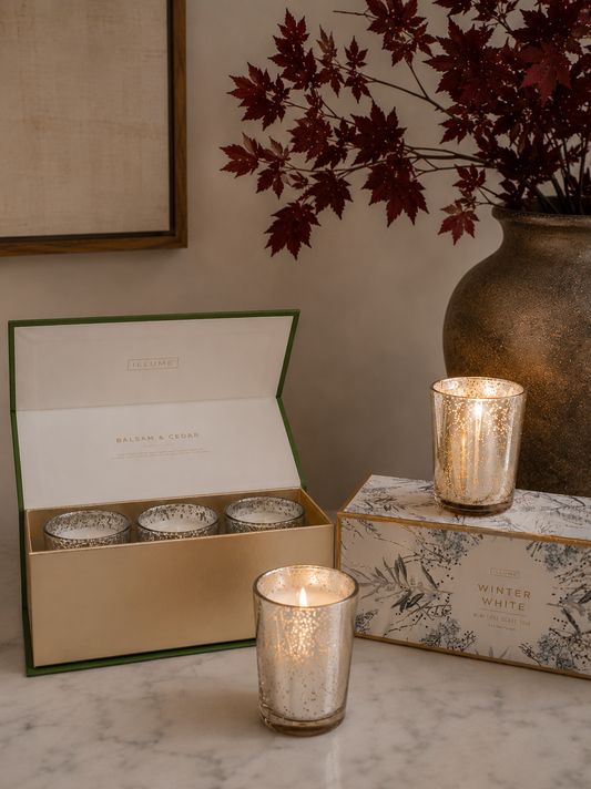 Mercury glass candle gift sets styled on a marble console with lit gold mercury glass votives, unopened silver mercury glass candles in a gift box, and warm seasonal décor.