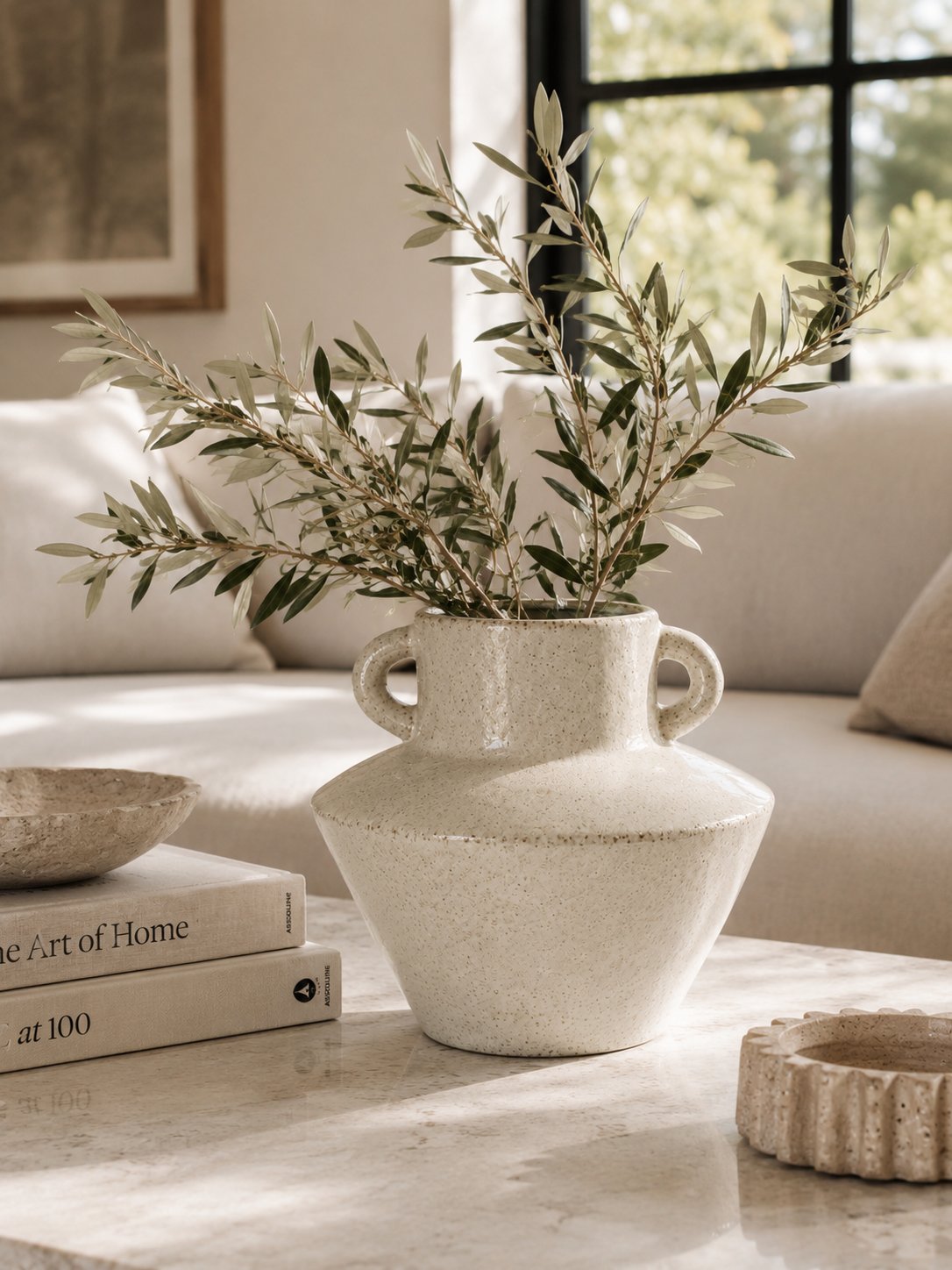 Speckled ivory ceramic vase with olive branches styled on marble coffee table in warm neutral California coastal living room