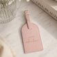 Katie Loxton Choose Adventure luggage tag in Dusty Pink faux leather styled on a neutral marble surface with elegant travel-inspired décor.
