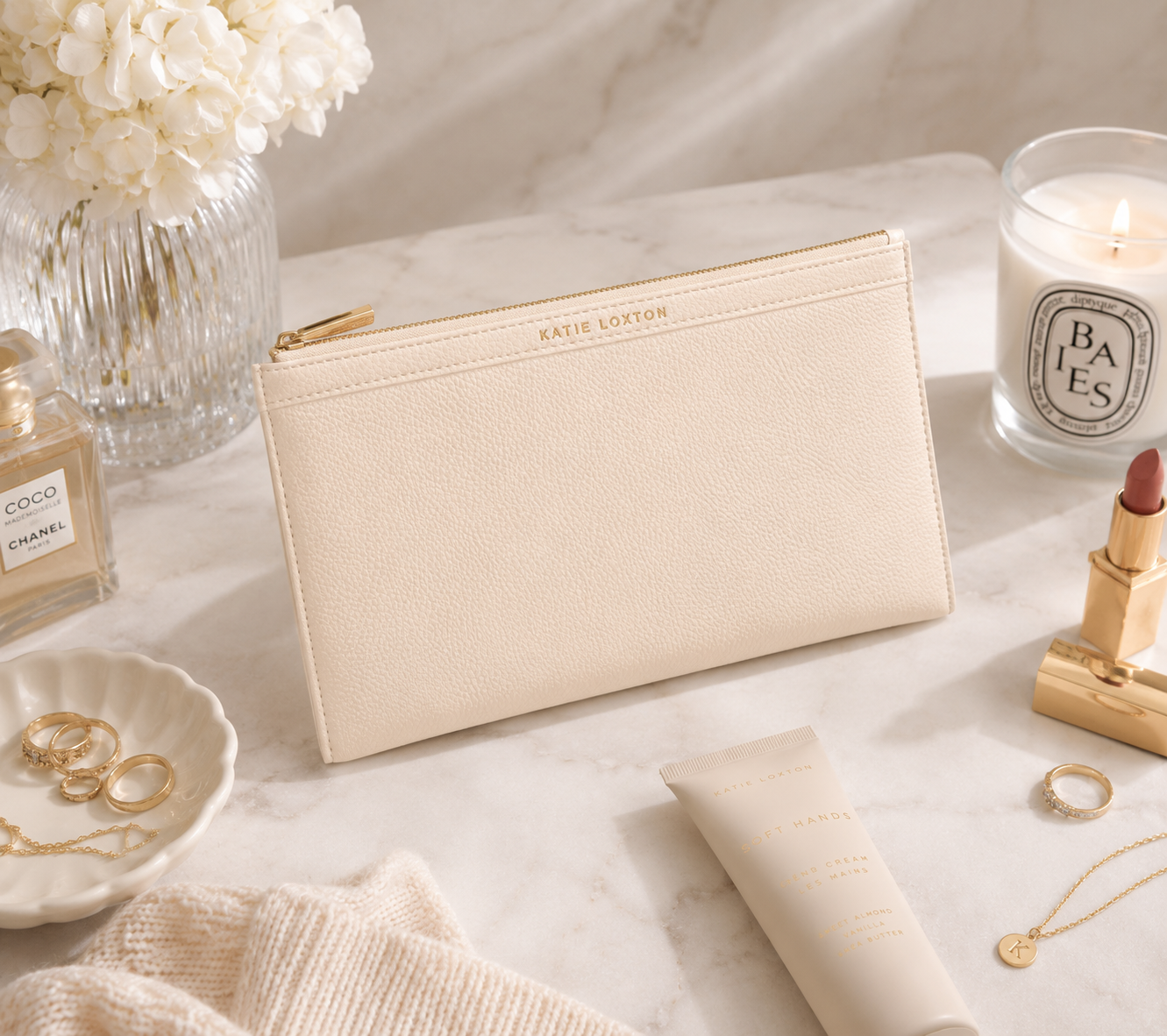 Katie Loxton Cleo Pouch in Eggshell faux leather styled on a marble vanity with beauty essentials, jewelry, and elegant neutral accessories.
