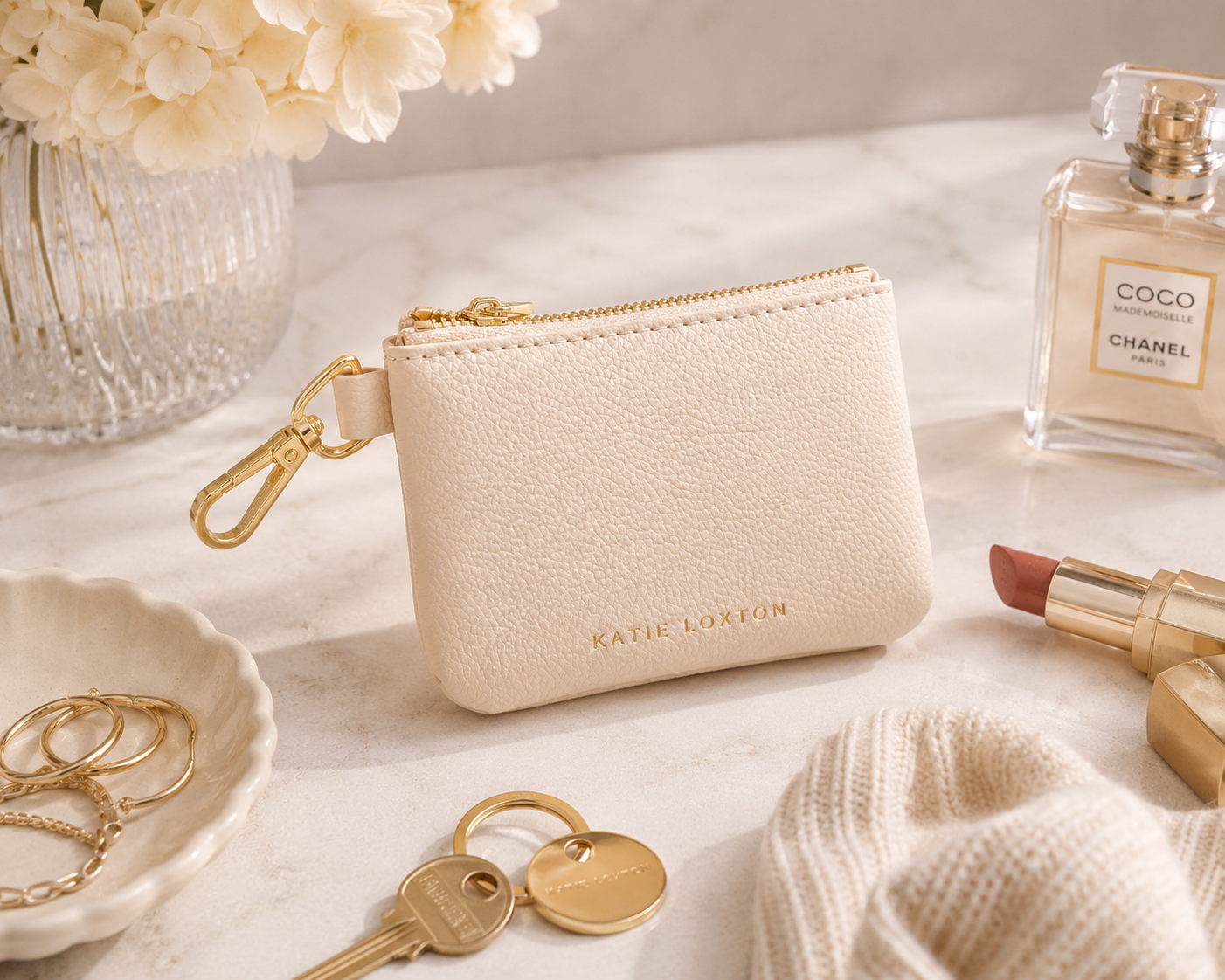 Katie Loxton Evie Clip-On Coin Purse in Eggshell faux leather styled with everyday essentials including keys, sunglasses, and jewelry on a neutral marble tabletop.