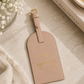 Katie Loxton Forever Exploring luggage tag in Soft Tan faux leather styled on a neutral tabletop with elegant travel accessories and soft natural lighting.