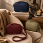 Katie Loxton Isla crossbody handbags in burgundy, navy, and sage green styled in a warm neutral living room with luxury editorial decor, soft lighting, and modern organic interiors.