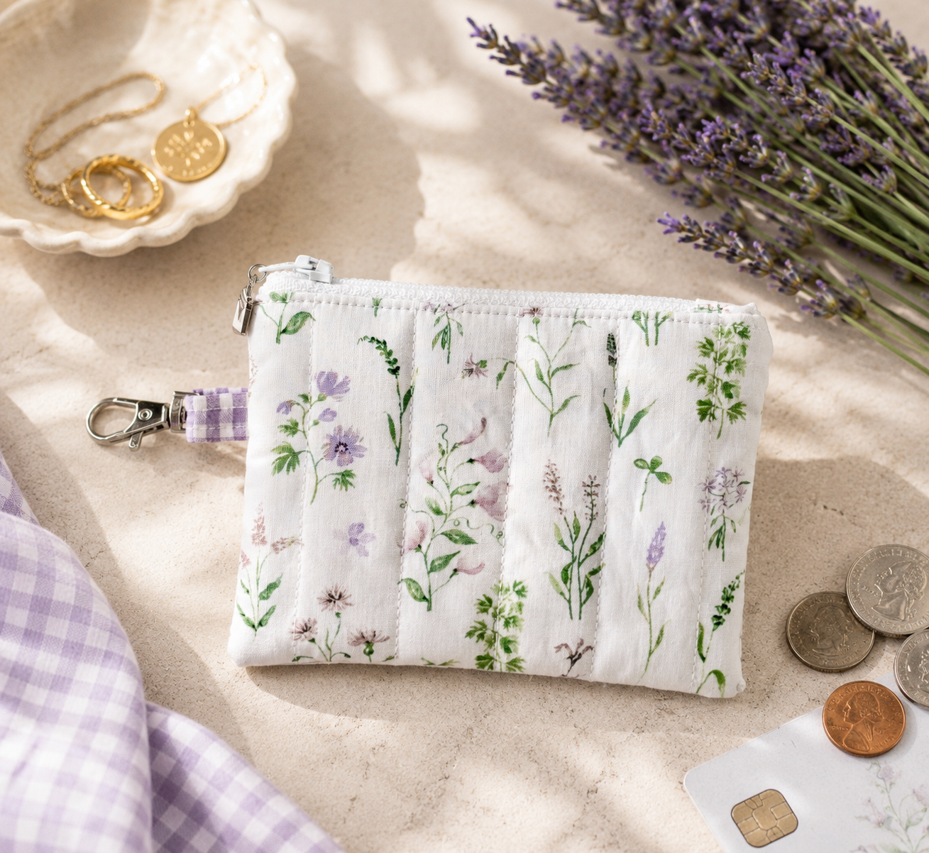 Lavender Meadows quilted coin purse with wildflower print and purple gingham loop styled with coins and everyday essentials.