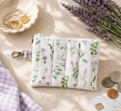 Lavender Meadows quilted coin purse with wildflower print and purple gingham loop styled with coins and everyday essentials.