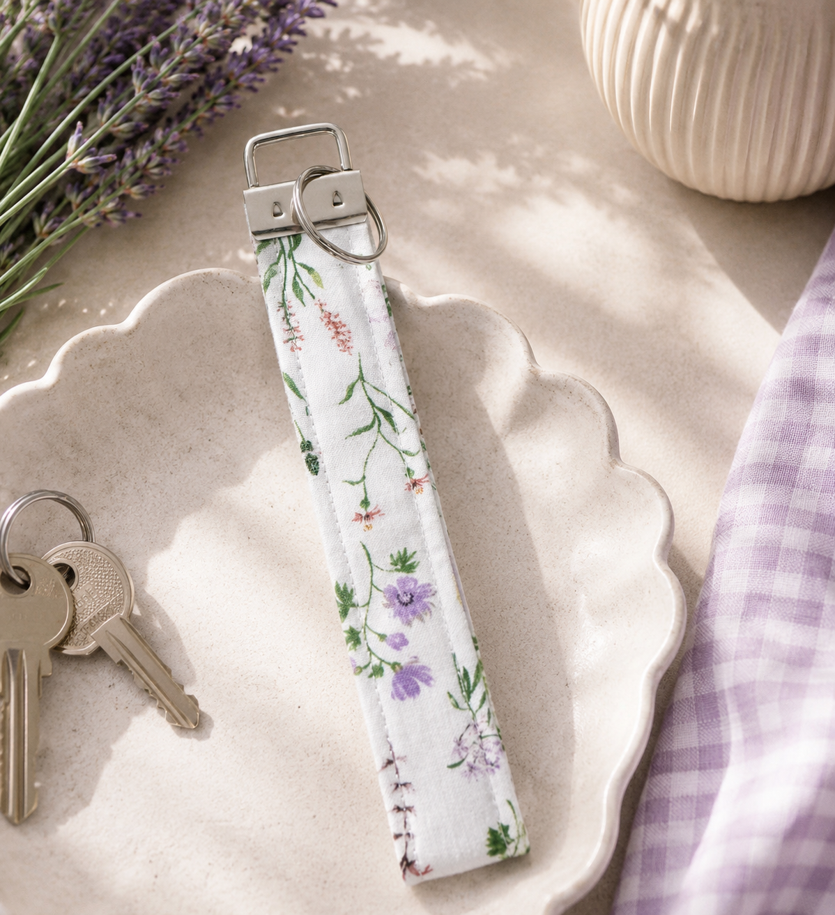 Lavender Meadows floral key fob wristlet with purple gingham accent styled with keys, sunglasses, and a neutral handbag.