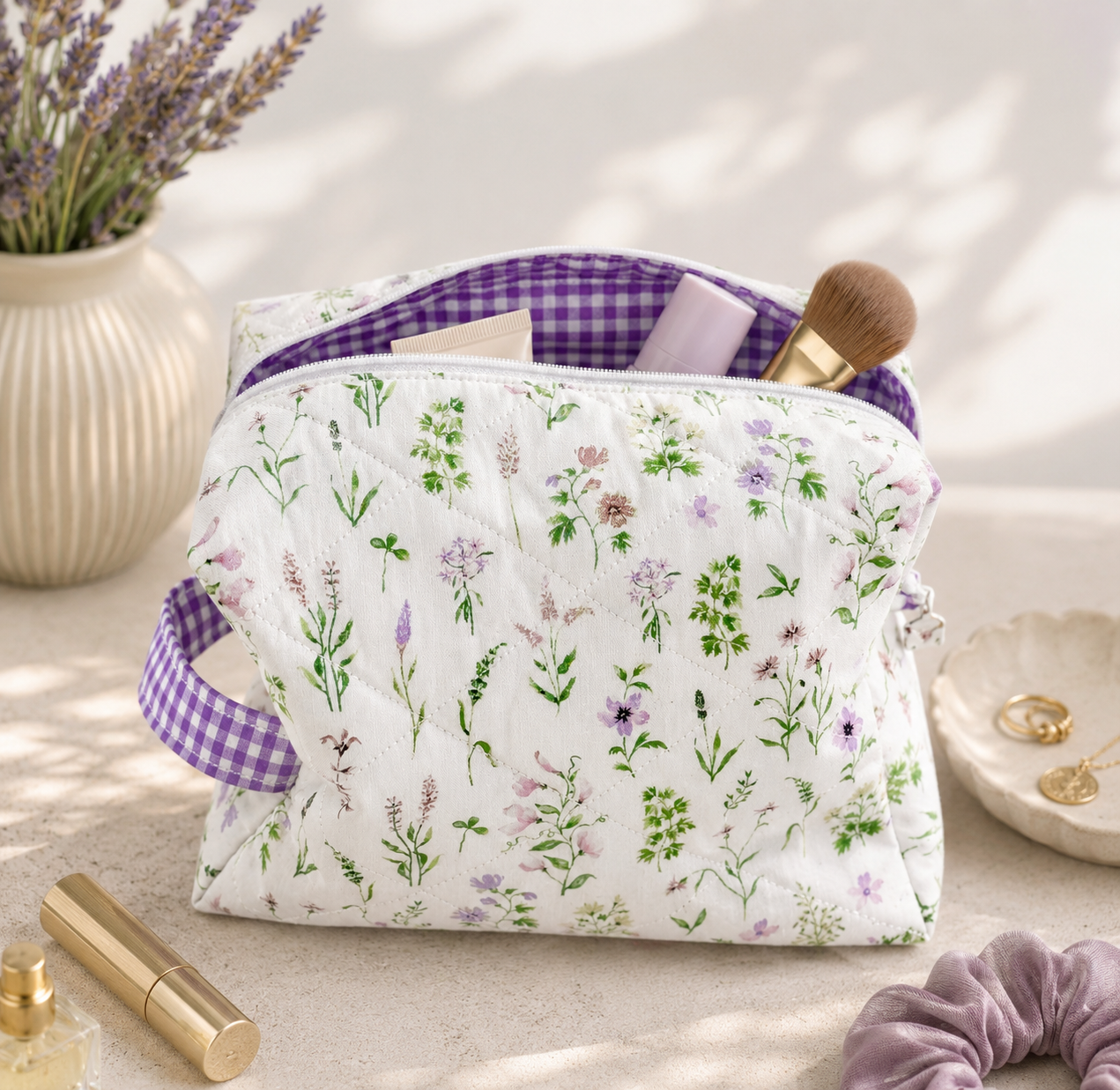 Lavender Meadows quilted makeup bag with wildflower print and purple gingham lining styled on a vanity with everyday beauty essentials.