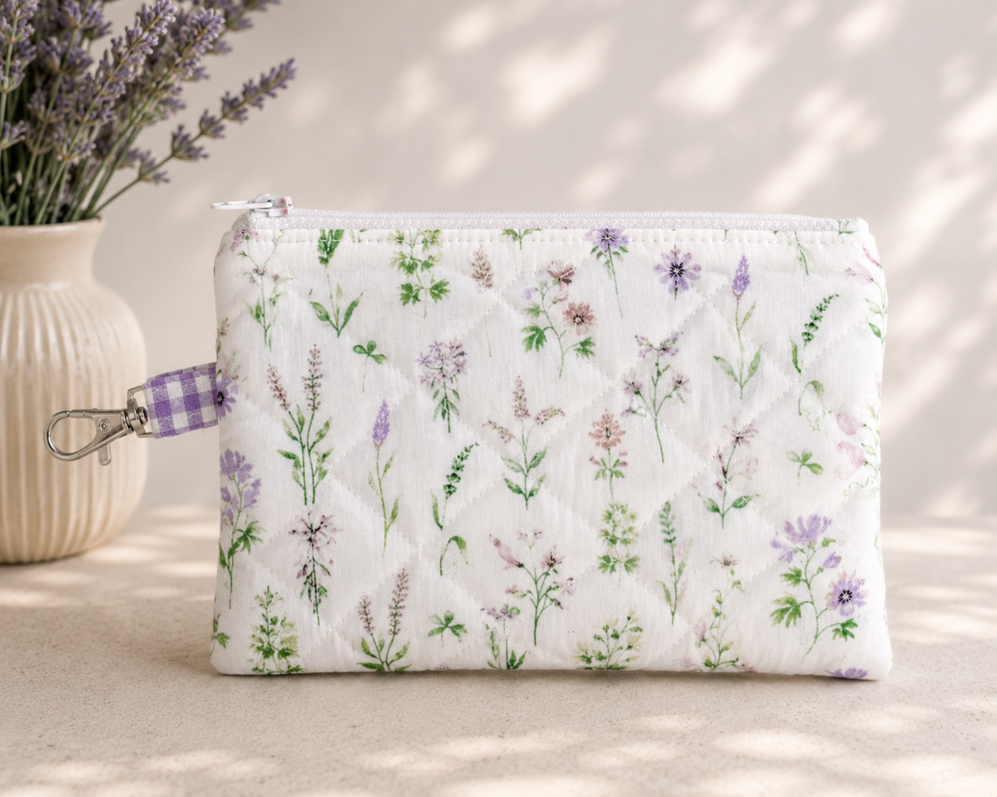 Lavender Meadows quilted medium wristlet pouch with wildflower print and purple gingham loop styled on a neutral tabletop with everyday accessories.