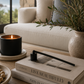 Matte black candle snuffer styled on a wood coffee table beside a lit candle, decorative bowl, and greenery in a modern California-inspired living room.