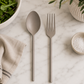 Matte gray stainless steel salad servers displayed on a white marble surface in a minimalist studio setting.
