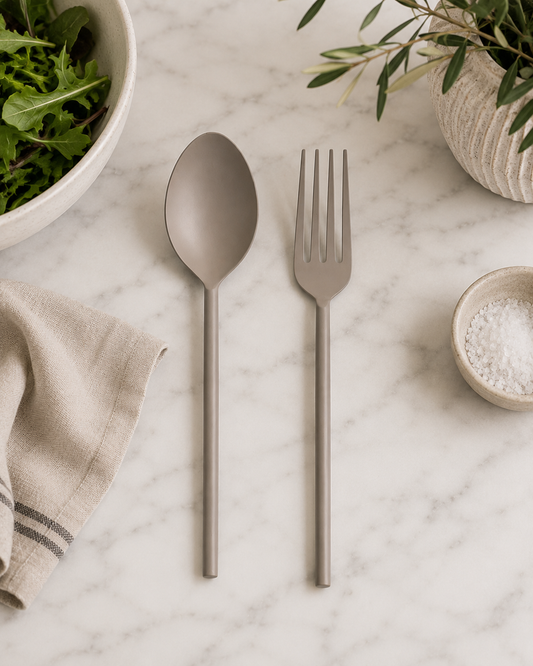 Matte gray stainless steel salad servers displayed on a white marble surface in a minimalist studio setting.