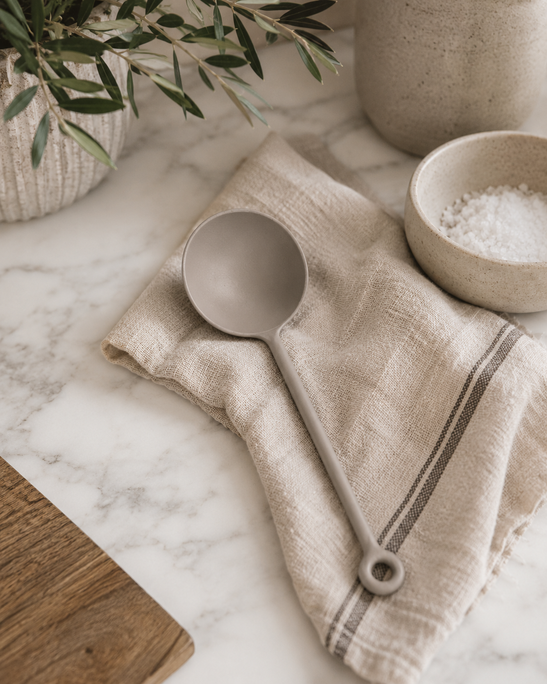 Matte gray stainless steel scoop styled on a marble countertop with a neutral linen towel, ceramic salt bowl, and modern California-inspired kitchen décor.